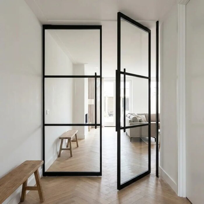Pair of black steel pivot doors with glass between hallway and living room, on an oak herringbone floor Pair of black steel pivot doors with glass between hallway and living room, on an oak herringbone floor