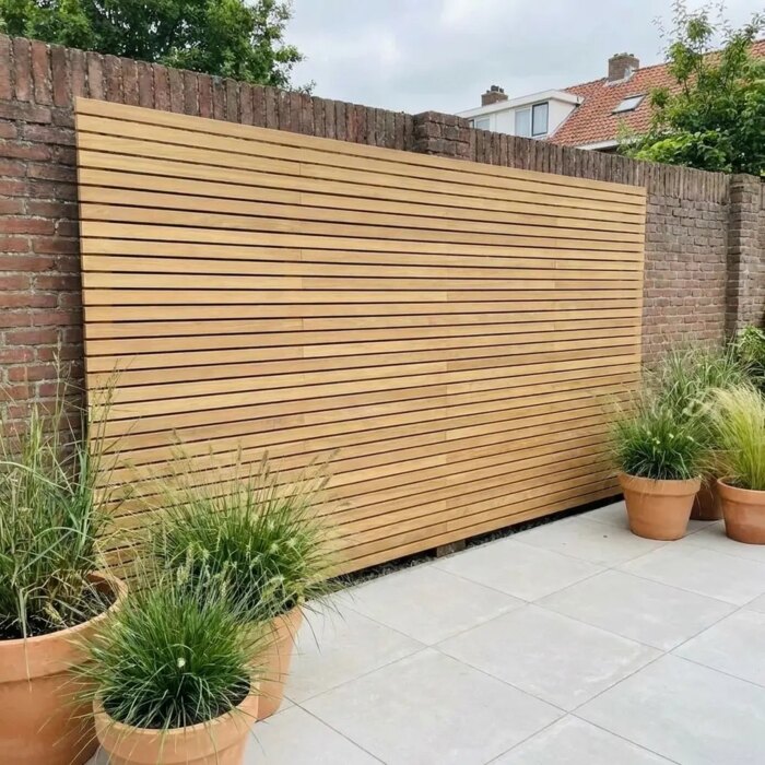 Single sided teak slatted fence in front of an old brick garden wall, with pots of ornamental grass on the patio Single sided teak slatted fence in front of an old brick garden wall, with pots of ornamental grass on the patio