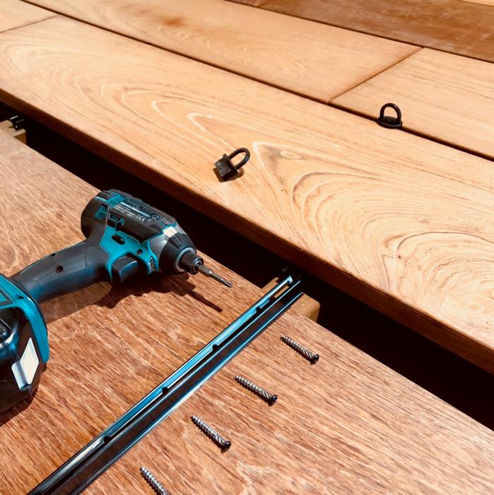 Professional installation of hardwood decking boards using black fastening strips and screws
