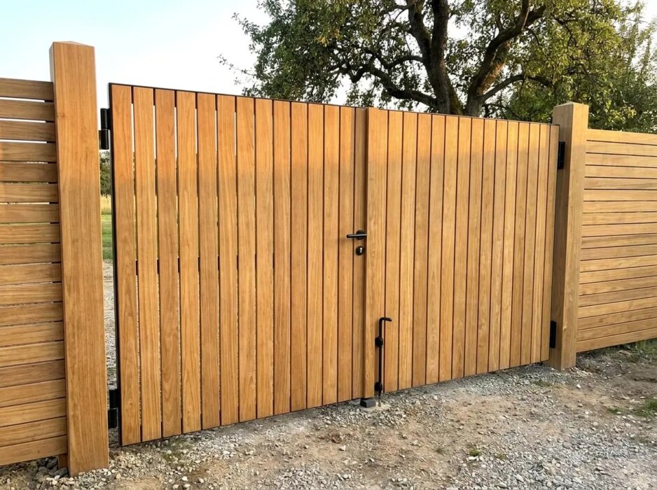 Double teak gate at a country house with a gravel drive and an old pear tree