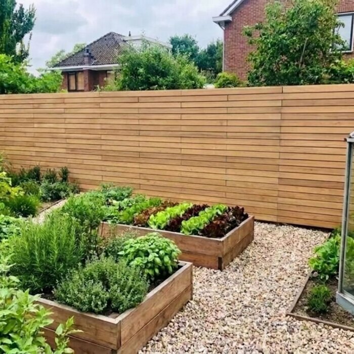 Round the kitchen garden: Teak fence with 7 cm slats behind raised vegetable beds and a greenhouse