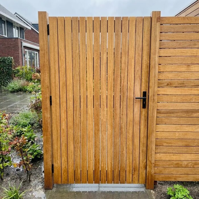 Teak garden gate with wide 90 mm slats after a shower, next to a teak fence