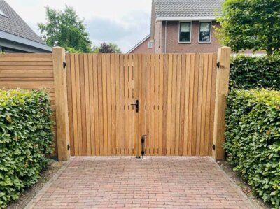 Double teak garden gate at the end of a brick paved driveway