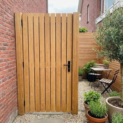 Teak gate with 90 mm slats in a courtyard garden with a brick wall and olive tree