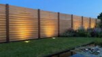 Teak fence with 7 cm slats lit by ground spotlights beside a pond at dusk