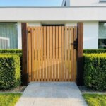 Teak garden gate with 70 mm slats in the front garden of a modern white house