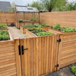 Teak gate with 70 mm slats in a teak fence around a vegetable garden with greenhouse