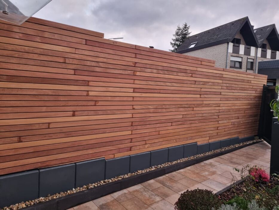 Modern slatted timber fence with height variation, installed in a stepped design for sloped gardens